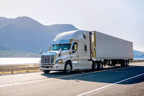 White semi truck with a refrigerated reefer trailer driving on the highway past mountains